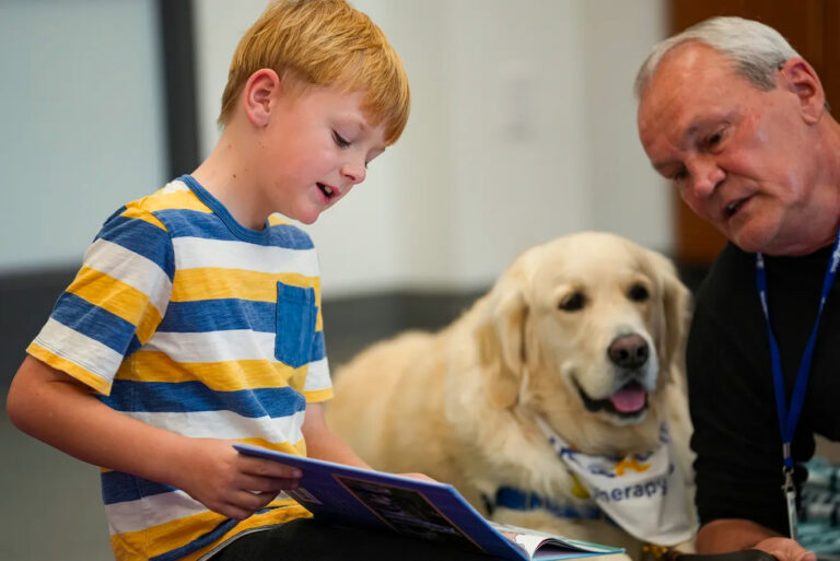 Photo of a boy reading a book to a Paws & Think therapy dog